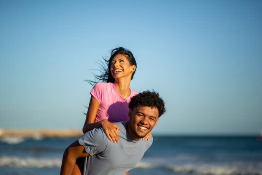 Happy young woman enjoying piggyback ride from boyfriend on sunny beach
