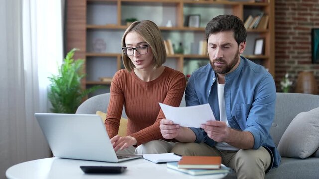 Couple paying bills online, planning financial budget, savings, calculating payments while sitting at home office. Husband and wife paying invoices using app on laptop computer, easy money management
