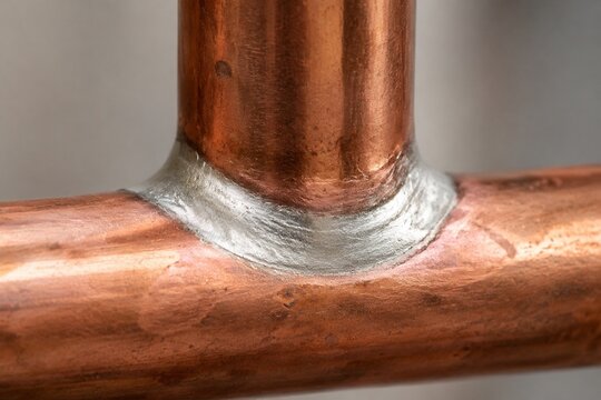 Close-up of a copper pipe joint with a silvery-white brazed connection.