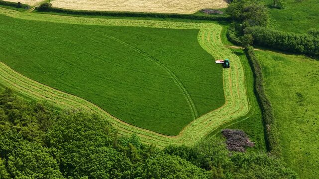 Satisfying Aerial View of Tractor Mowing Green Field in Pattern in English countryside in spring. Agricultural industries, commercial landscaping, rural lifestyle. 4K.