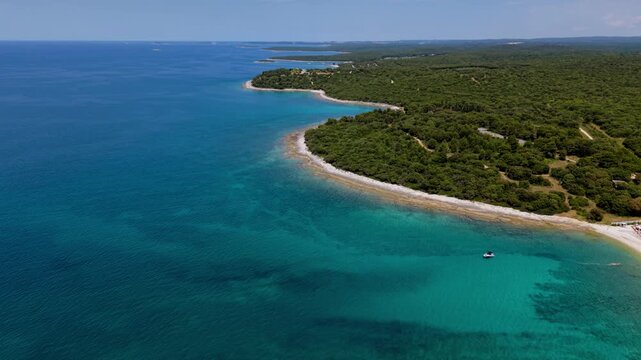 Small yacht boat floating in a turquoise Adriatic bay near Pula, Croatia. Pine forest and pebble beach, aerial view.
