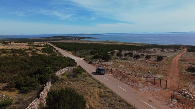 Aerial follow a camping van as it travels an empty country road toward the ocean on pag Island, Croatia