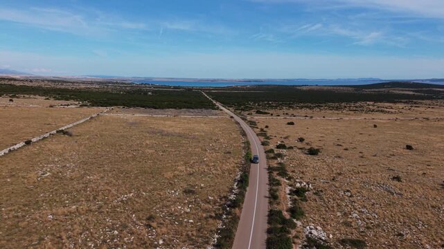 Camping van from above, driving along coastal highway on Pag Island, Croatia. Aerial car follow