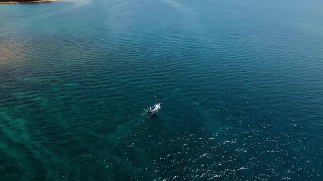 White sailboat cruising along the green coast of Pula, Croatia. Sunny day, aerial tracking shot.