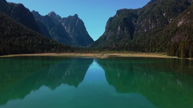 Spectacular reflection of alpine peaks in the still, turquoise water of Toblachsee lake, aerial shot
