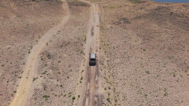 Modern camper van navigating a remote gravel road through the barren stone desert of Pag island. Aerial
