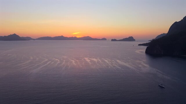 Wide drone shot of rippled tropical water and distant islands glowing beneath an orange horizon