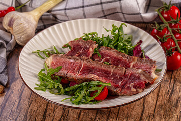 Fototapeta premium Sliced steak with arugula and cherry tomatoes on rustic plate