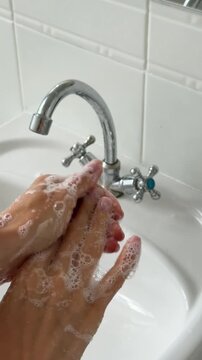 Detailed shot of soapy hands rubbing together under running water in a sink.
