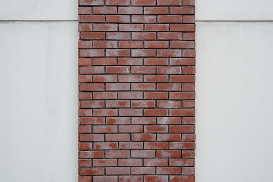 Minimalist architectural background showing a single vertical red brick column embedded in a smooth white wall with copy space