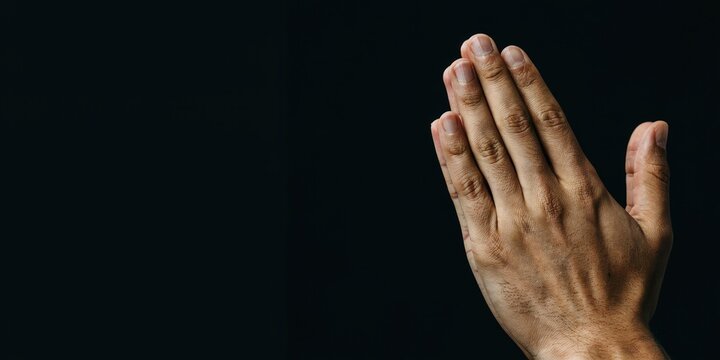Close-up of human hands pressed together in prayer against a black background