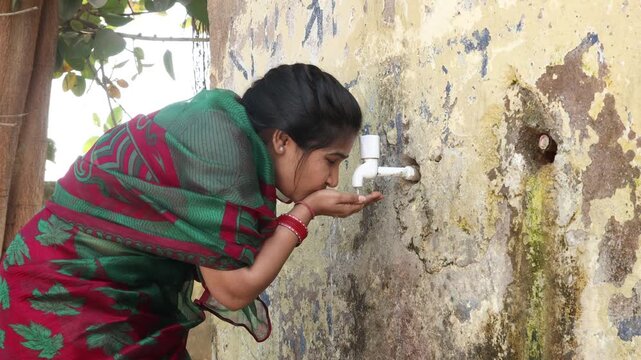 Young Indian thirsty woman drinking fresh clean water from tap in hot summer. concept of hydration, South Asia water crisis  Heat wave, Rural india life.  Climate change. 