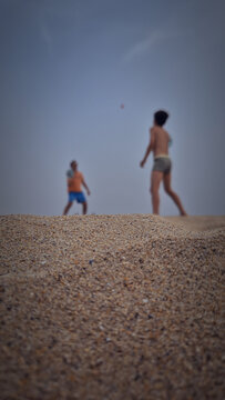 Two people playing beach paddleball on the sand, blurred in the background with copy space and a low-angle summer vacation concept.