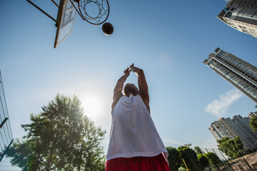 Obraz premium Young athletic man showcases skills while shooting hoops on sunny day