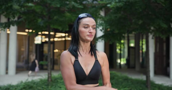 Young beautiful woman athlete in sportswear training and jumping rope in an urban park among high-rise buildings and trees