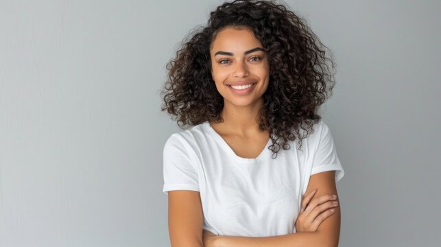 Smiling mixed race woman with curly hair looking at the camera with crossed arms.