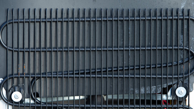 Close-up of refrigerator condenser coils and black cooling grid texture.  A detailed close-up shot capturing the black metal condenser coils and grid structure on the back of a domestic refrigerator.