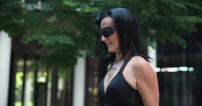 Young beautiful woman athlete in sportswear training and jumping rope in an urban park among high-rise buildings and trees