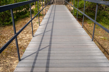 Obraz premium Wooden boardwalk path with metal handrails in sunny nature park. Travel and hiking concept. Real Photo