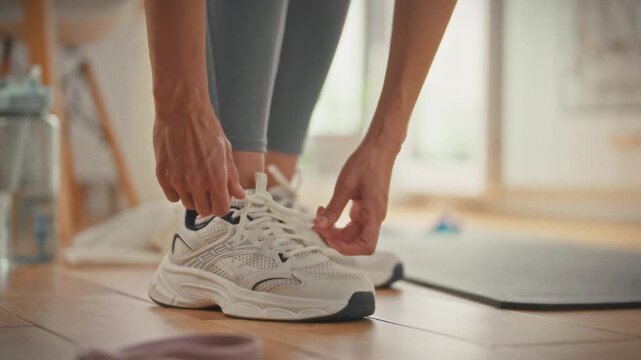 An athlete prepares for training by tying her sneakers at home during the day. The concept of starting the path to a healthy lifestyle and regular physical activity at home