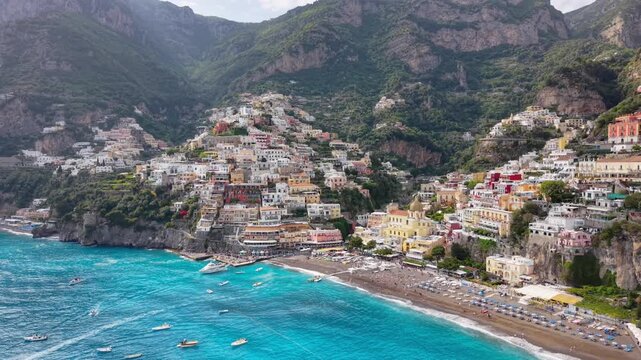Aerial Drone Low Lateral View of Positano with Crowded Beach, Chiesa Santa Maria Assunta and Vivid Blue Sea, Amalfi Coast Italy Summer