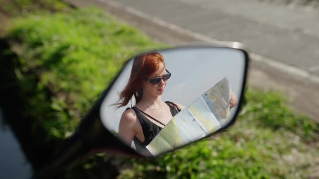 Woman traveler looking at map reflected in scooter mirror