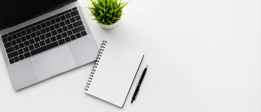 Laptop keyboard with blank notebook and pen on white desk with green plant for workspace concept