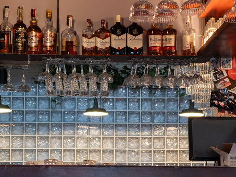 Kyiv, Ukraine - March 21, 2026: Premium Ballantine's, Jameson, Chivas, and Wild Turkey liquor bottles displayed on a modern dark wooden bar shelf with elegant hanging wine glasses