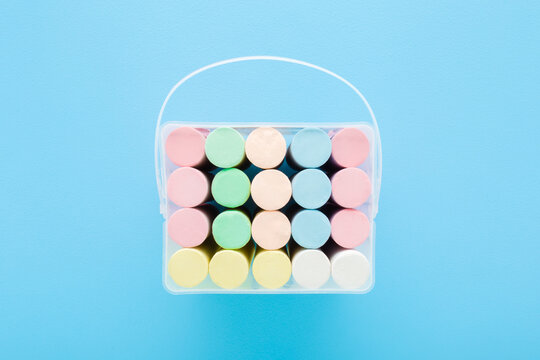 Opened plastic box with new colorful chalk sticks on light blue table background. Pastel color. Closeup. Flat lay. Top down view.