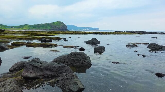 Low angle pan revealing black volcanic rocks in clear tide pool and Hamori Layer green tuff platform at Sagye Beach near Yongmeori in Jeju, South Korea