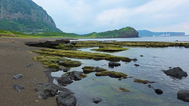 Rising reveal over Hamori Layer green tuff rock platform and tide pools at Sagye Beach with Yongmeori headland and calm bay in Jeju, South Korea