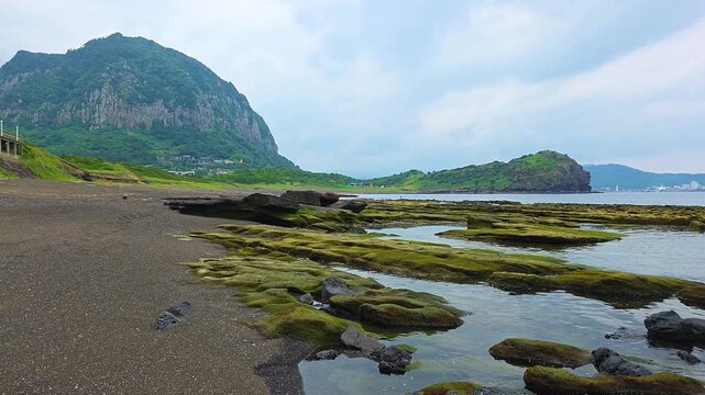 Wide view of Hamori Layer green tuff rock platform and tide pools at Sagye Beach below Sanbangsan mountain and Yongmeori headland in Jeju, South Korea
