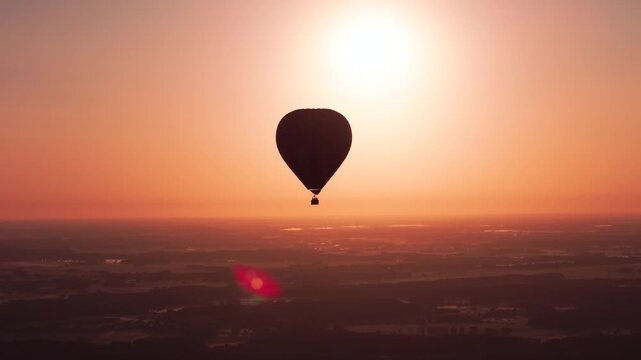 A cinematic wide shot of a hot air balloon silhouette drifting peacefully above a rural landscape during a vibrant orange sunset. Perfect for travel and wellness content.