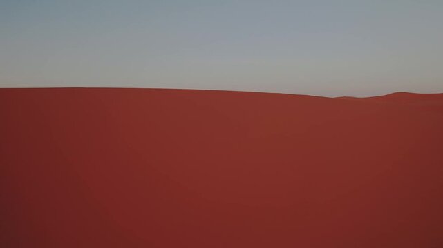 Towering Erg Chebbi dune rises above the Sahara near Merzouga, Errachidia, Dr&acirc;a-Tafilalet, Morocco, Africa, glowing with warm sunset tones, drone lateral slide and yaw shot.