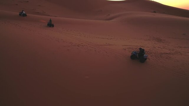 Quad bikes traverse the Erg Chebbi dunes near Merzouga, Errachidia, Dr&acirc;a-Tafilalet, Morocco, Africa, leaving tracks across the Sahara during warm sunset light, drone pan tracking shot.
