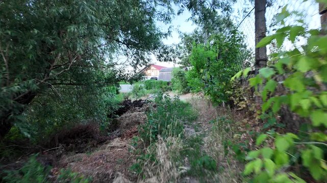 Walking down the scenic dirt path past dry summer grass and lush green trees toward a beautiful country house with a prominent red roof. Amazing cinematic stock shot in 4K 24fps with Motion Blur.