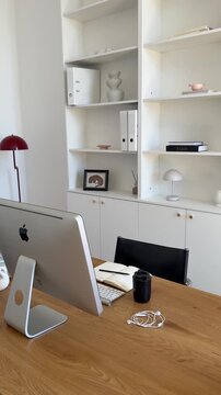 Elegant workspace showing a desktop computer on a wooden desk with white minimalist shelves