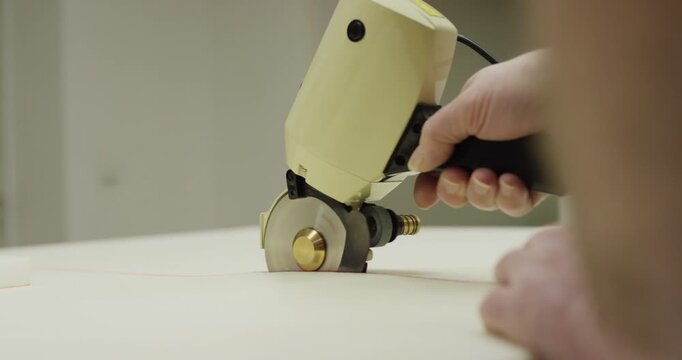 A hand operates a circular blade electric cutter to slice through a thick piece of foam