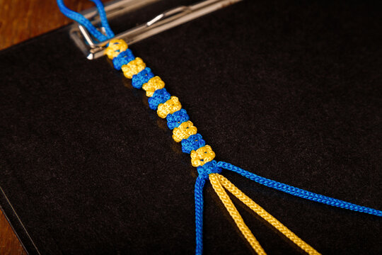 Making process of macrame wristband, paracord bracelet in national Ukrainian flag colors - blue yellow on black background. DIY workshop