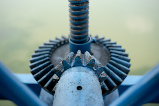 Close up macro view of blue painted bevel gears and threaded rod mechanism of heavy machinery