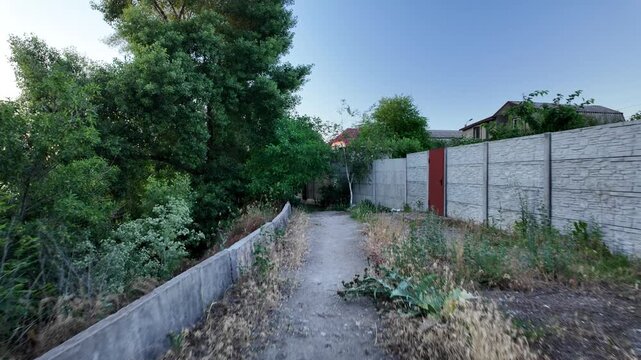 Walking down the scenic dirt path past dry summer grass and lush green trees toward a beautiful country house with a prominent red roof. Amazing cinematic stock shot in 4K 24fps with Motion Blur.