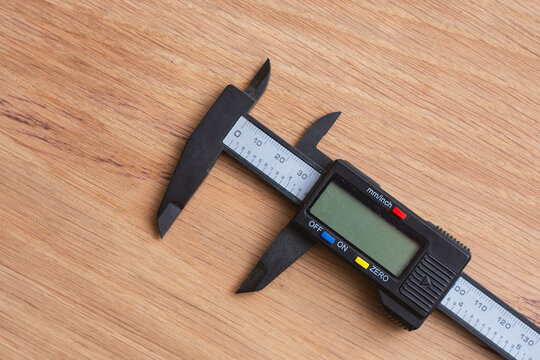 Digital caliper on a wooden surface for technical or industrial design. Precision measuring tool for engineering, machining, quality control, manufacturing, woodworking and workshop applications.