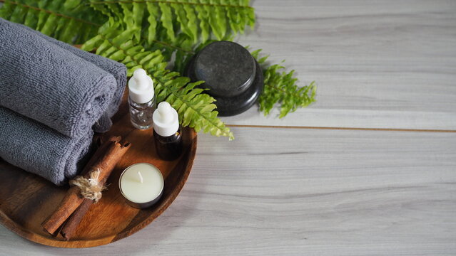 Luxury spa arrangement with gray towels, massage stones, body oil, candle, cinnamon sticks and fresh greenery. Wellness, relaxation, aromatherapy, self care and natural skincare concept with copy spac