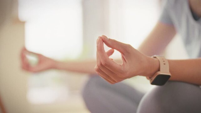 On a sunlit floor at home, a girl sits cross-legged in lotus on her yoga mat, hands pressed in mudra, practicing meditation and mindfulness. The serene pose fosters deep relaxation and inner calm