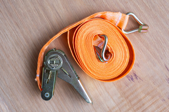 Ratchet tie down strap with metal hooks and tension mechanism on a wooden surface. Cargo securing, load restraint, transportation safety, moving, logistics and trailer equipment concept.