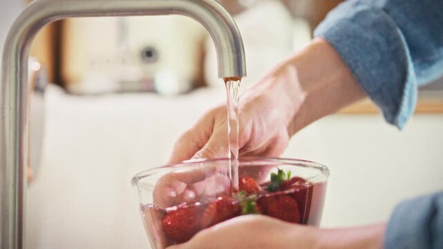 Ripe strawberries in a man's hands are washed with a large bowl of water before preparing a dessert. Concept of preparing sweet dishes at home with fresh summer berries