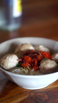 A bowl of traditional Indonesian beef meatballs with noodles, rice vermicelli, savory broth, chili sauce, and sweet soy sauce.