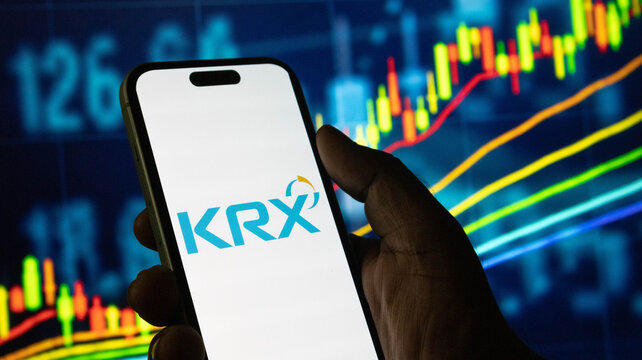 Korea exchange (KRX) logo on smartphone screen with financial graphs in background.