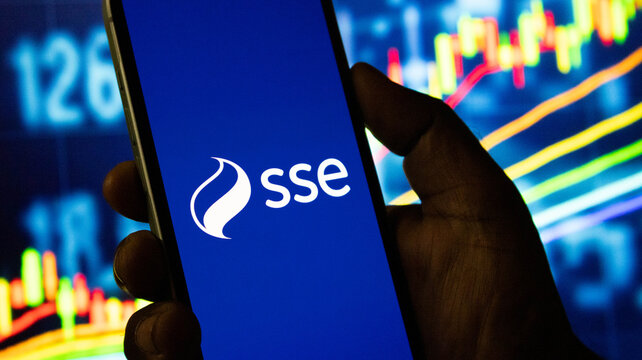 Mobile phone with sse logo on blue background held by hand against stock market analytics.