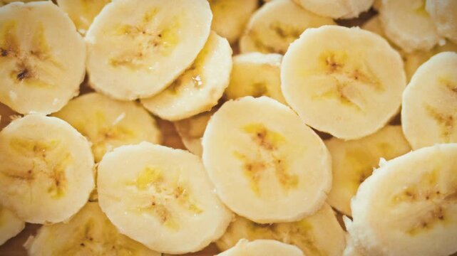Thin yellow banana slices are loosely stacked in multiple layers, forming textured backdrop that highlights fruit's ripe color and natural grain. The arrangement emphasizes fresh, unprocessed produce